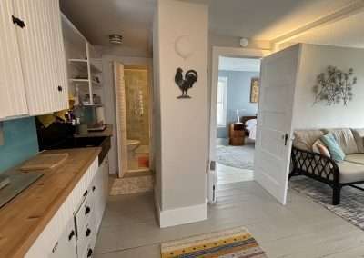 Kitchenette with dishware in cabinets, full sink, view of bathroom and bedroom.